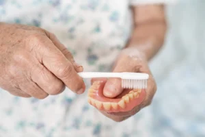 denture care and maintenance showing an elderly patient gently brushing a partial denture to keep it clean and in good condition